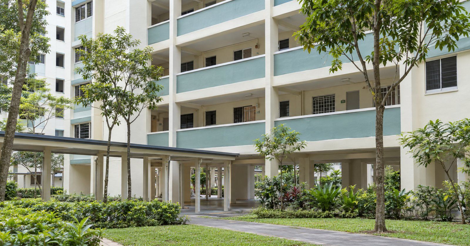 Pale cream and teal HDB-style blocks beside a sheltered walkway and trees in daylight